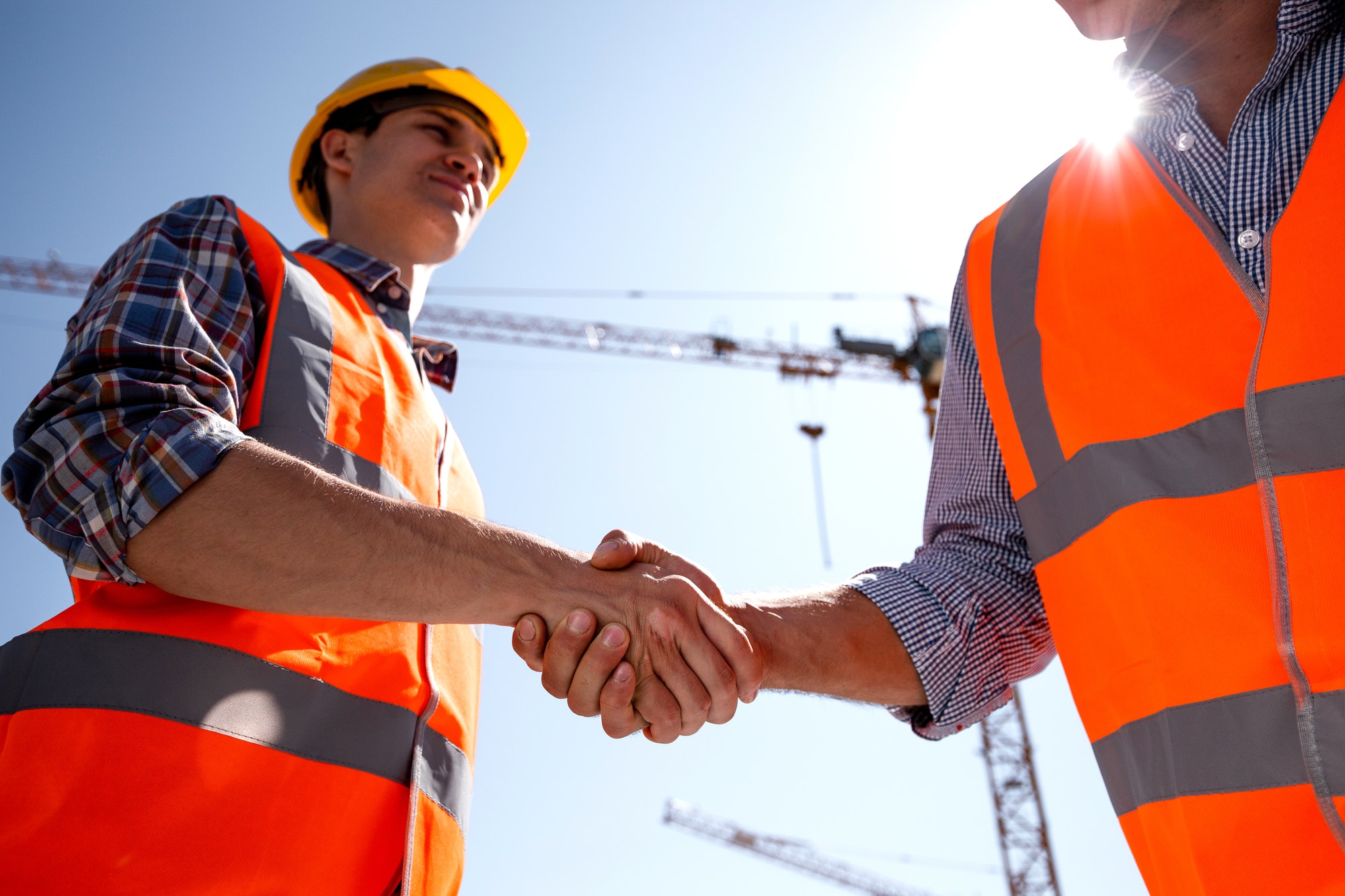 structural-engineer-and-architect-dressed-in-orange-work-vests-and-helmets-shake-hands-on-the